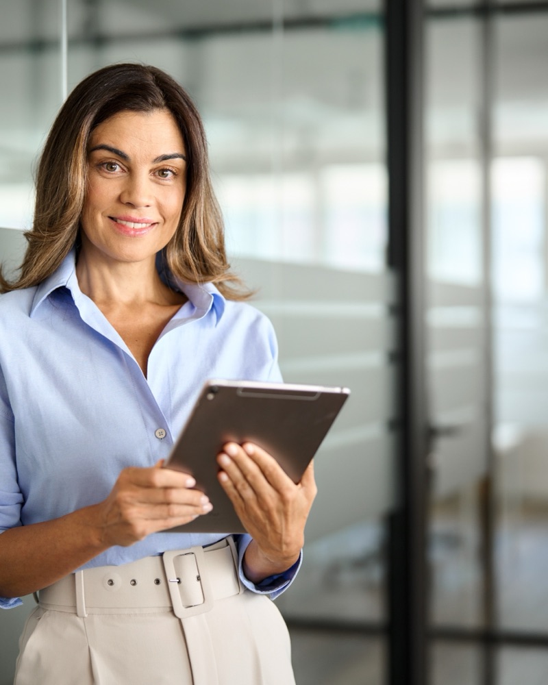 Smiling woman looking at her phone while using laptop to book a trip